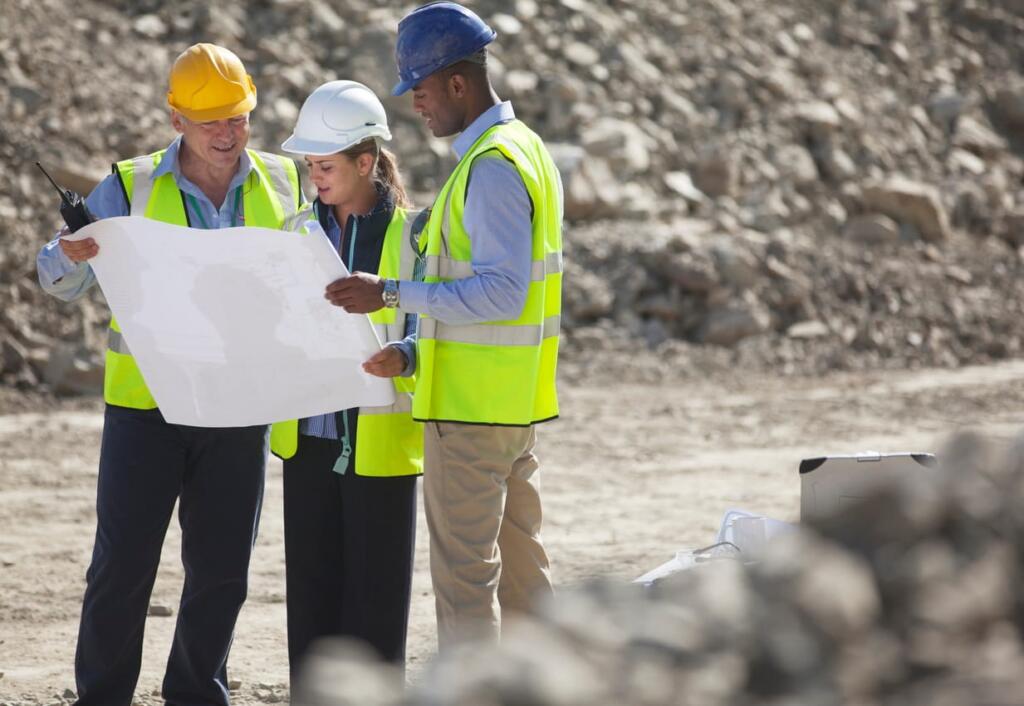 Three construction workers are looking at blueprints on a job site.