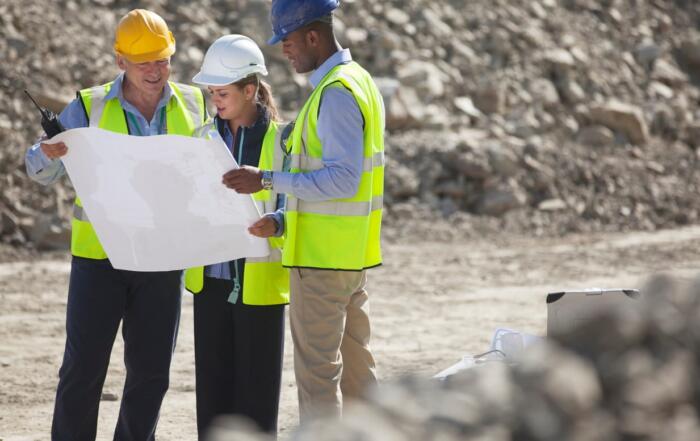 Three construction workers are looking at blueprints on a job site.