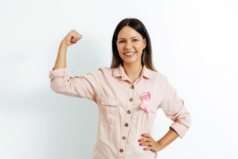 A breast cancer survivor wears a pink ribbon and is showing off arm muscles to signify she beat cancer. 