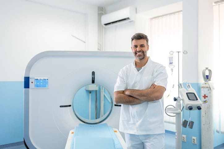 A doctor smiling and standing next to a CT scanner. 