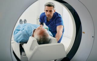 A Male Nurse Is Assisting An Elderly Male Patient Into A Ct Scanner To Screen For Lung Cancer.