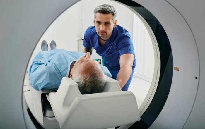 A male nurse is assisting an elderly male patient into a CT scanner to screen for lung cancer.