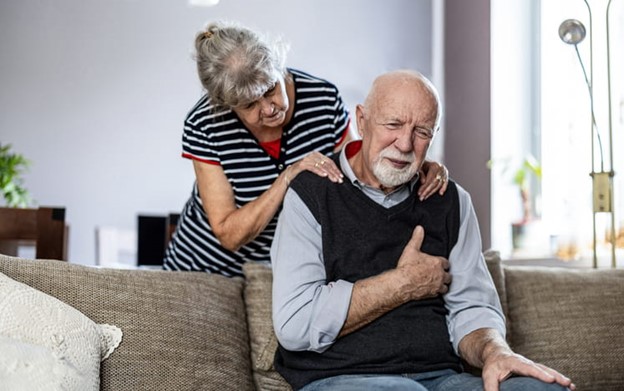 man feeling heart pain sitting on couch with wife comforting him