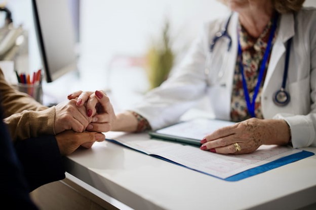 Female doctor reaching across desk to hold hands of two people