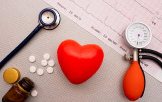 A Stethoscope And Blood Pressure Cuff, Along With A Fake Heart And Pills, Lay On Top Of Ekg Results.