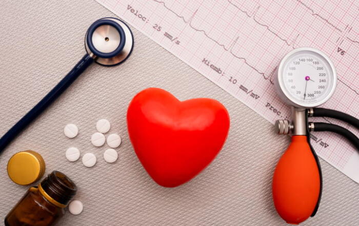 A Stethoscope And Blood Pressure Cuff, Along With A Fake Heart And Pills, Lay On Top Of Ekg Results.