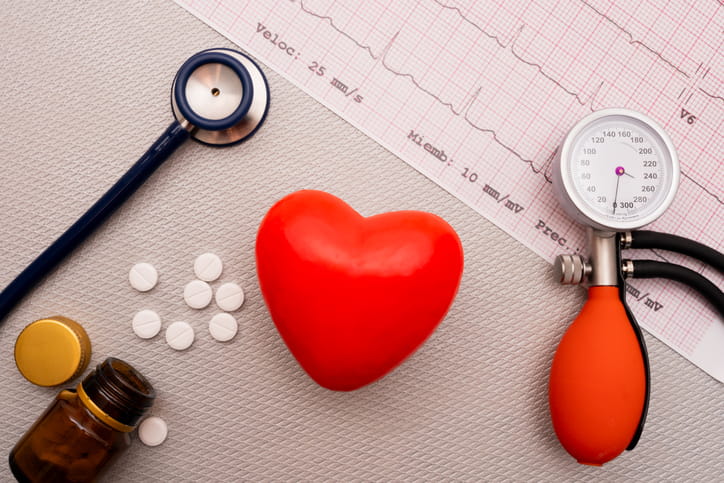 A Stethoscope And Blood Pressure Cuff, Along With A Fake Heart And Pills, Lay On Top Of Ekg Results. 