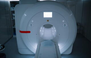 A Modern Mri Scanner In A Dimly Lit, Blue-Toned Hospital Room, With The Patient Table Extended Forward From The Machine'S Central Tunnel.