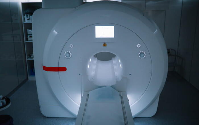 A Modern Mri Scanner In A Dimly Lit, Blue-Toned Hospital Room, With The Patient Table Extended Forward From The Machine'S Central Tunnel.