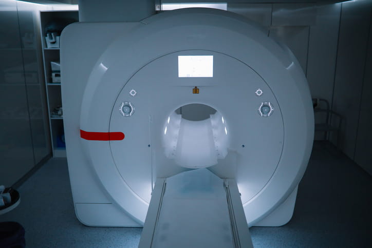 A Modern Mri Scanner In A Dimly Lit, Blue-Toned Hospital Room, With The Patient Table Extended Forward From The Machine'S Central Tunnel.