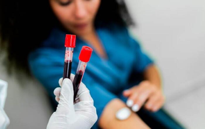 Pdc Home 2 A Close-Up Of A Doctor Holding Two Blood Collection Tubes With The Patient Blurred Out In The Background.